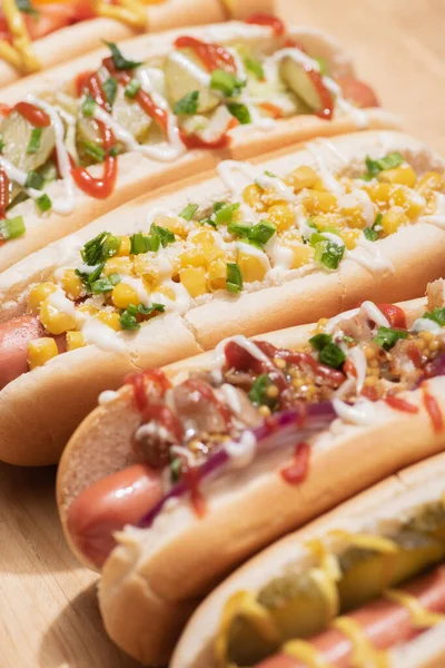 Fuoco selettivo di vari deliziosi hot dog freschi con verdure e salse sulla tavola di legno — Foto stock