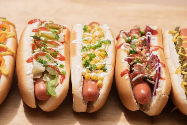 Vários cachorros-quentes saborosos frescos com verduras e molhos na mesa de madeira — Fotografia de Stock