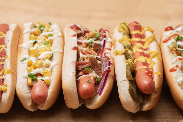 Vários cachorros-quentes saborosos frescos com verduras e molhos na mesa de madeira — Fotografia de Stock