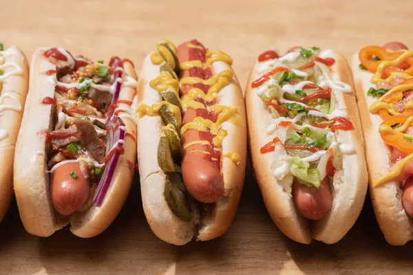 Fresh various tasty hot dogs with vegetables and sauces on wooden table — Stock Photo