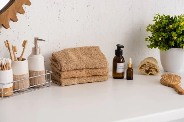 Estante con objetos de higiene cerca de toallas, productos de belleza y maceta en el baño, concepto de cero residuos - foto de stock