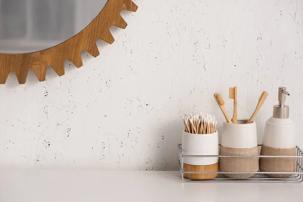 Estante con jabón líquido, porta cepillos de dientes con cepillos de dientes y orejeras cerca del espejo en el baño, concepto de cero residuos - foto de stock