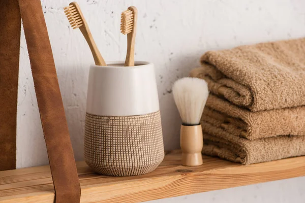 Vista de cerca del estante con soporte para cepillo de dientes con cepillos de dientes, toallas y cepillo de afeitar en el baño, concepto de cero residuos - foto de stock