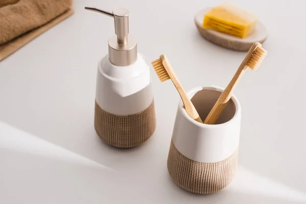 Close up view of liquid soap, toothbrush holder with toothbrushes, towels and dish with soap on grey, zero waste concept — Stock Photo