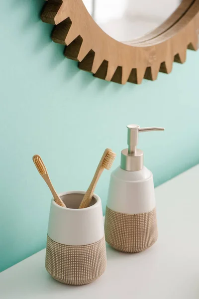Soporte de cepillo de dientes con cepillos de dientes y jabón líquido cerca de espejo redondo en la pared en el baño, concepto de cero residuos - foto de stock
