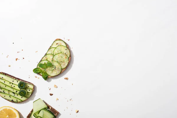 Top view of fresh cucumber toasts with seeds, mint and basil leaves and lemon on white background — Stock Photo