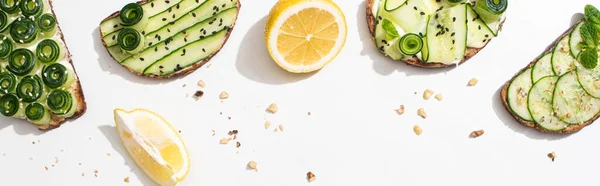 Top view of fresh cucumber toasts with seeds, mint and basil leaves and lemon on white background, panoramic shot — Stock Photo