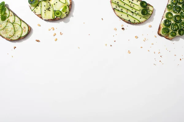 Draufsicht auf frische Gurken-Toasts mit Samen, Minze und Basilikumblättern auf weißem Hintergrund — Stockfoto