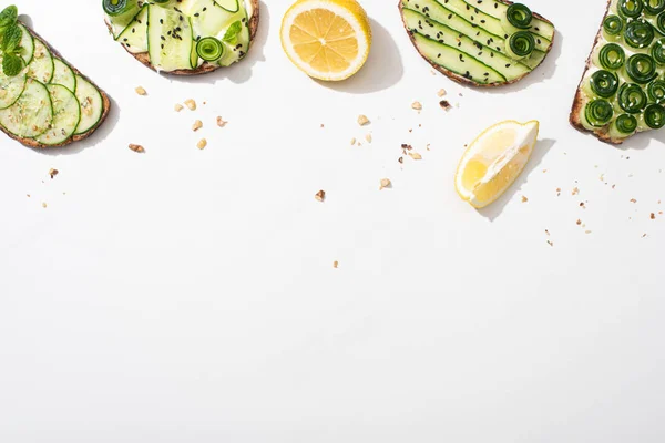 Top view of fresh cucumber toasts with seeds, mint and basil leaves and lemon on white background — Stock Photo