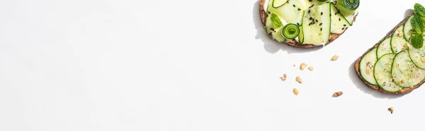 Draufsicht auf frische Gurken-Toasts mit Samen, Minze und Basilikumblättern auf weißem Hintergrund, Panoramaaufnahme — Stockfoto