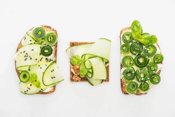 Vue de dessus des toasts de concombre frais avec des graines et des feuilles de basilic isolées sur blanc — Photo de stock