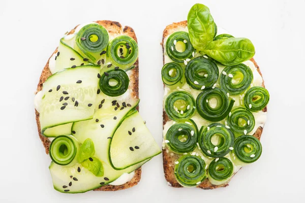 Vista superior de tostadas frescas de pepino con semillas y hojas de albahaca aisladas en blanco - foto de stock