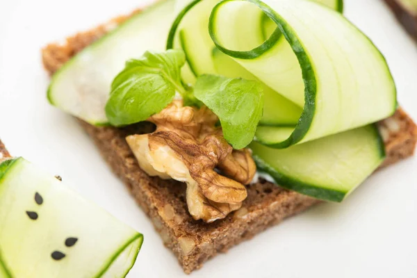 Vista de cerca de la tostada de pepino fresco con nuez y hojas de albahaca aisladas en blanco - foto de stock