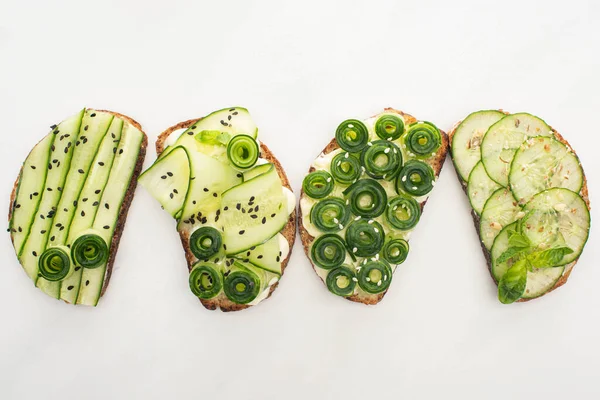 Vue de dessus des toasts au concombre frais avec des graines, de la menthe et des feuilles de basilic sur fond blanc — Photo de stock