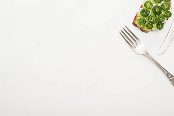 Вид на свежий огуречный тост с семенами и столовыми приборами на белом фоне — стоковое фото