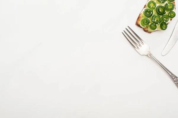 Vista superior de la tostada de pepino fresco con semillas y cubiertos sobre fondo blanco - foto de stock