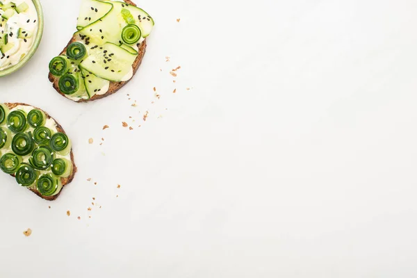 Draufsicht auf frische Gurken-Toasts mit Samen, Basilikumblätter in der Nähe von Joghurt in Schüssel auf weißem Hintergrund — Stockfoto