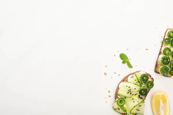 Top view of fresh cucumber toasts with seeds, mint and basil leaves and lemon on white background — Stock Photo