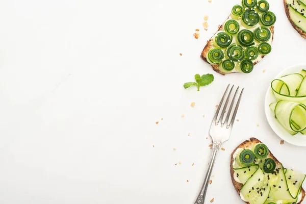 Vista dall'alto di toast di cetrioli freschi con semi, foglie di menta e forchetta su sfondo bianco — Foto stock