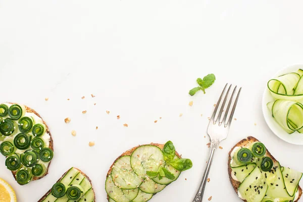 Top view of fresh cucumber toasts with seeds, mint and basil leaves and fork on white background — Stock Photo