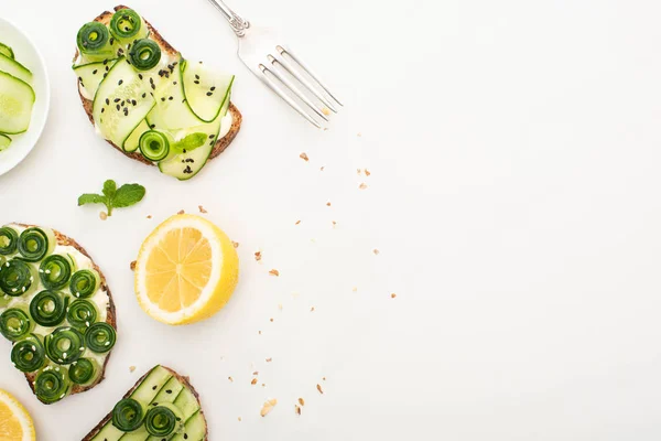 Top view of fresh cucumber toasts with seeds, mint leaves near lemon and fork on white background — Stock Photo