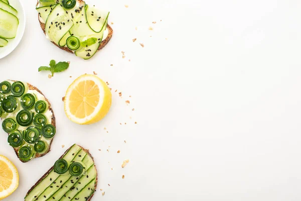 Top view of fresh cucumber toasts with seeds, mint leaves near lemon on white background — Stock Photo