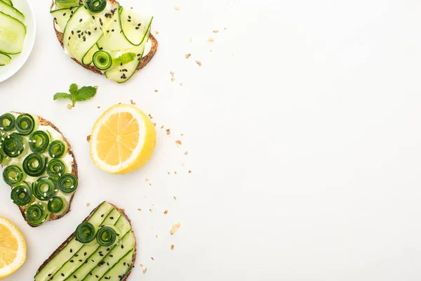 Vista superior de tostadas de pepino fresco con semillas, hojas de menta cerca de limón sobre fondo blanco - foto de stock