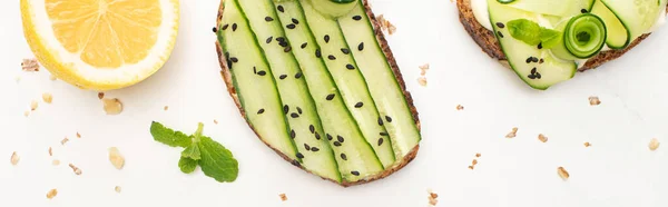 Top view of fresh cucumber toasts with seeds, mint leaves near lemon on white background, panoramic shot — Stock Photo