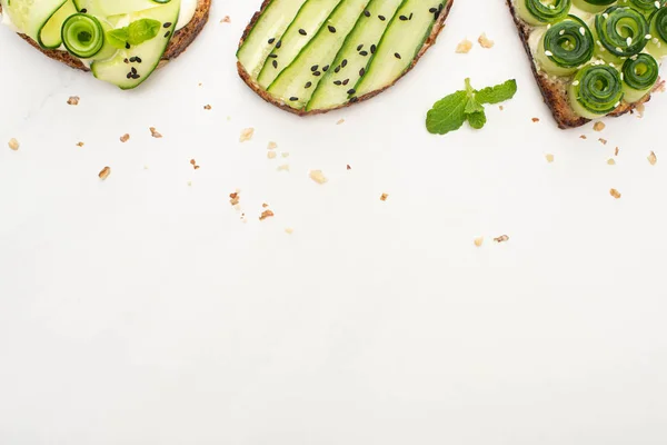 Vue de dessus des toasts au concombre frais avec des graines, feuilles de menthe sur fond blanc — Photo de stock