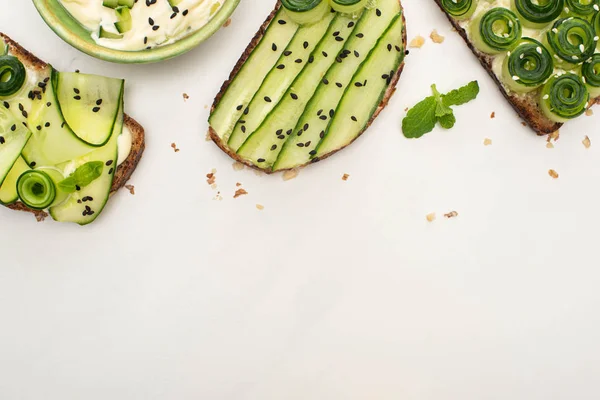 Vue de dessus des toasts de concombre frais avec des graines, feuilles de menthe près du yaourt sur fond blanc — Photo de stock