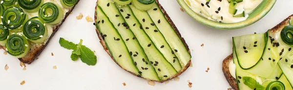 Top view of fresh cucumber toasts with seeds, mint leaves near yogurt on white background, panoramic shot — Stock Photo