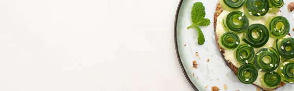 Top view of fresh cucumber toast with sesame and mint leaves on plate on white background, panoramic shot — Stock Photo