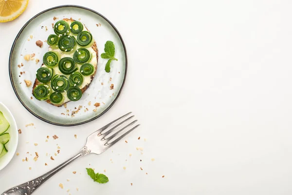 Draufsicht auf frischen Gurkentoast mit Sesam und Minzblättern auf Teller in der Nähe von Gabel und Zitrone auf weißem Hintergrund — Stockfoto