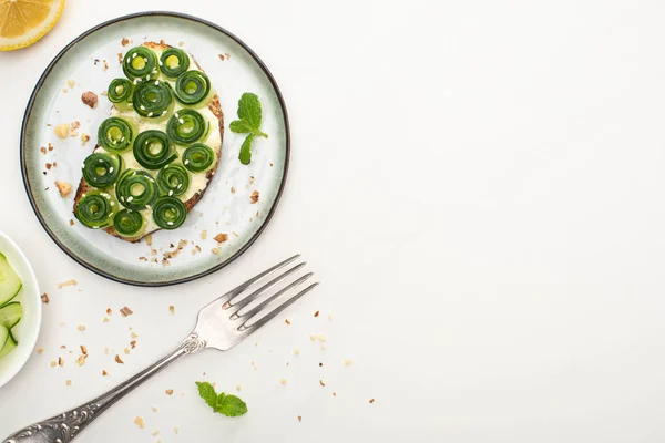 Top view of fresh cucumber toast with sesame and mint leaves on plate near fork and lemon on white background — Stock Photo