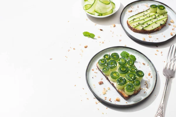 Frische Gurken-Toasts auf Tellern in der Nähe der Gabel auf weißem Hintergrund — Stockfoto