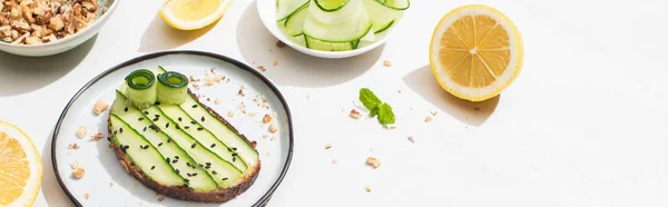 Pane tostato di cetriolo fresco con semi vicino a foglie di menta e limone su sfondo bianco, colpo panoramico — Foto stock