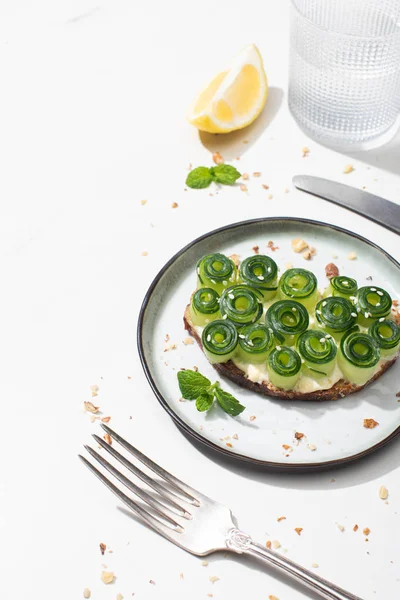 Tostadas de pepino fresco con semillas servidas con cubiertos, limón y agua sobre fondo blanco - foto de stock