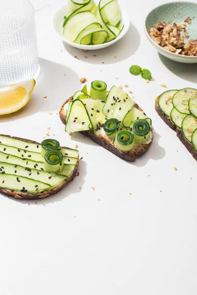 Fresh cucumber toasts with seeds, mint leaves and lemon near glass of water on white background — Stock Photo