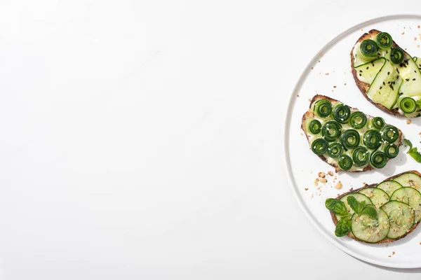 Top view of fresh cucumber toasts with seeds, mint and basil leaves on plate on white background — Stock Photo