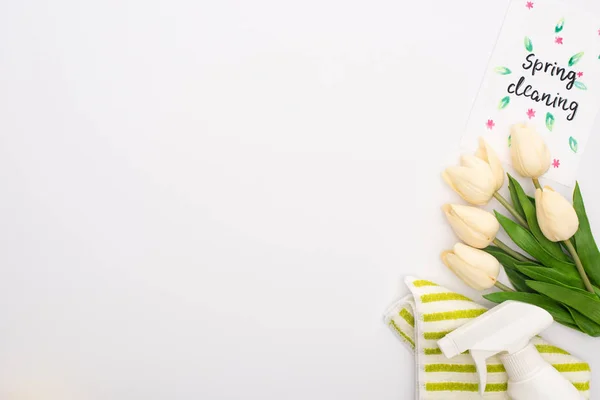 Top view of spring tulips and cleaning supplies near spring cleaning card on white background — Stock Photo