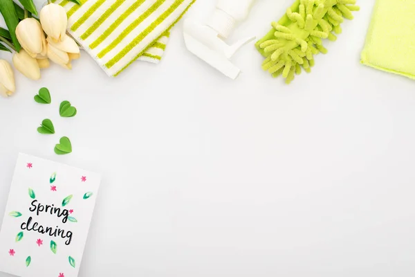 Top view of spring tulips and green cleaning supplies near spring cleaning card on white background — Stock Photo