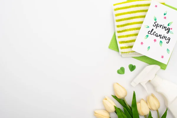 Top view of spring tulips and cleaning supplies near spring cleaning card on white background — Stock Photo