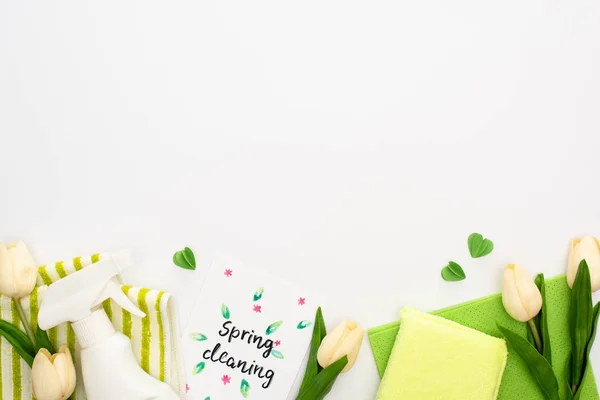 Top view of spring tulips and green cleaning supplies near spring cleaning card on white background — Stock Photo