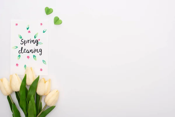 Vista superior de los tulipanes de primavera y corazones verdes cerca de la tarjeta de limpieza de primavera sobre fondo blanco - foto de stock