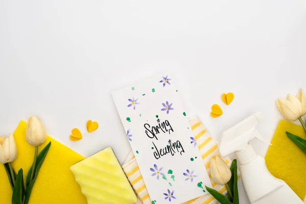 Top view of spring tulips and yellow cleaning supplies near spring cleaning card on white background — Stock Photo