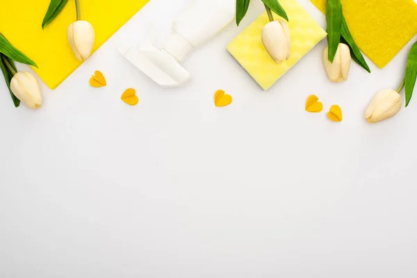 Top view of spring tulips and yellow cleaning supplies with hearts on white background — Stock Photo