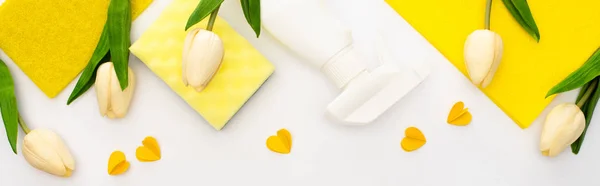 Top view of spring tulips and yellow cleaning supplies with hearts on white background, panoramic shot — Stock Photo