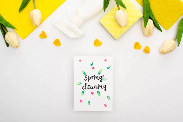 Top view of spring tulips and yellow cleaning supplies with hearts near spring cleaning card on white background — Stock Photo