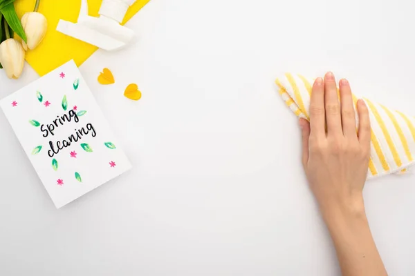 Cropped view of woman holding rag near spring tulips, yellow cleaning supplies, spring cleaning card on white background — Stock Photo