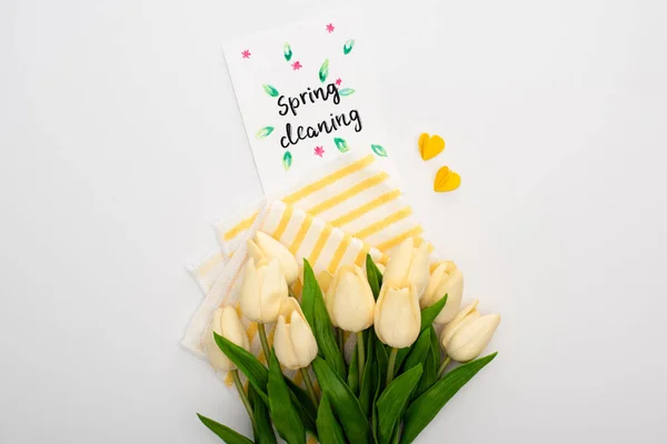 Vista superior de tulipas de primavera e suprimentos de limpeza amarela perto de cartão de limpeza de primavera no fundo branco — Fotografia de Stock